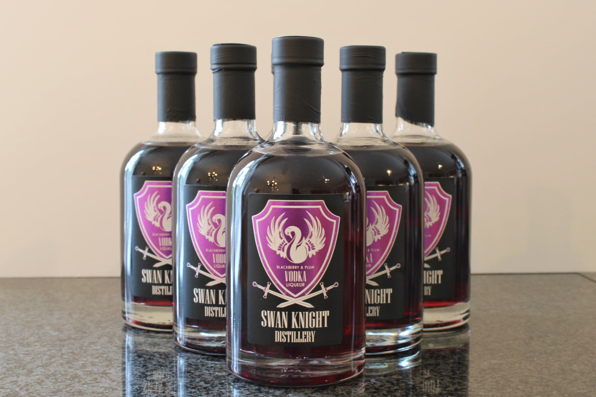 6 bottles of Swan Knight Distillery Blackberry and Plum Vodka Liqueur on a dark countertop.