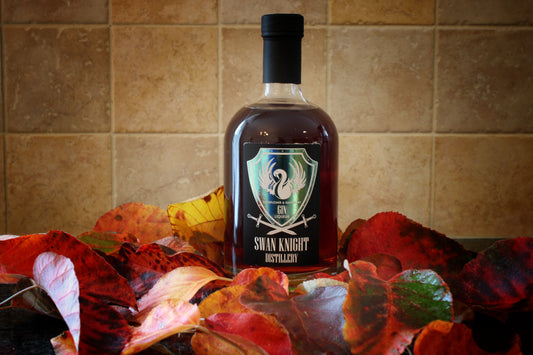 A bottle of Swan Knight Distillery Elderflower and Dark Berry Gin Liqueur nestled in a bed of leaves.