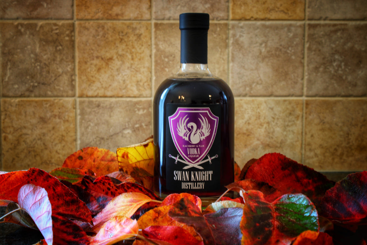 A bottle of Swan Knight Distillery Blackberry and Plum Vodka Liqueur nestled in a bed of leaves.