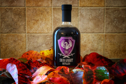 A bottle of Swan Knight Distillery Blackberry and Plum Vodka Liqueur nestled in a bed of leaves.