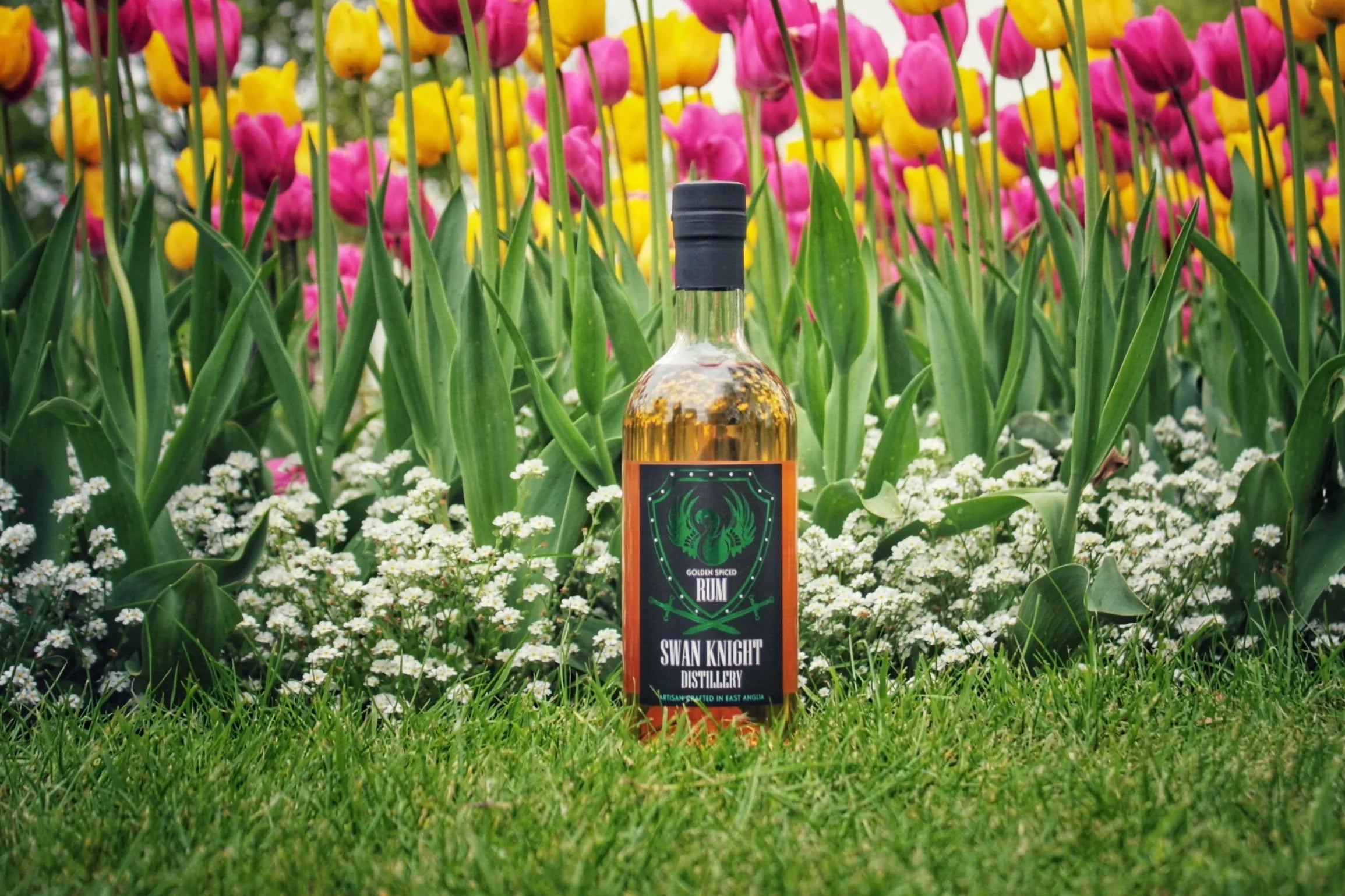 Bottle of Swan Knight Distillery golden spiced rum with a back drop of tulips