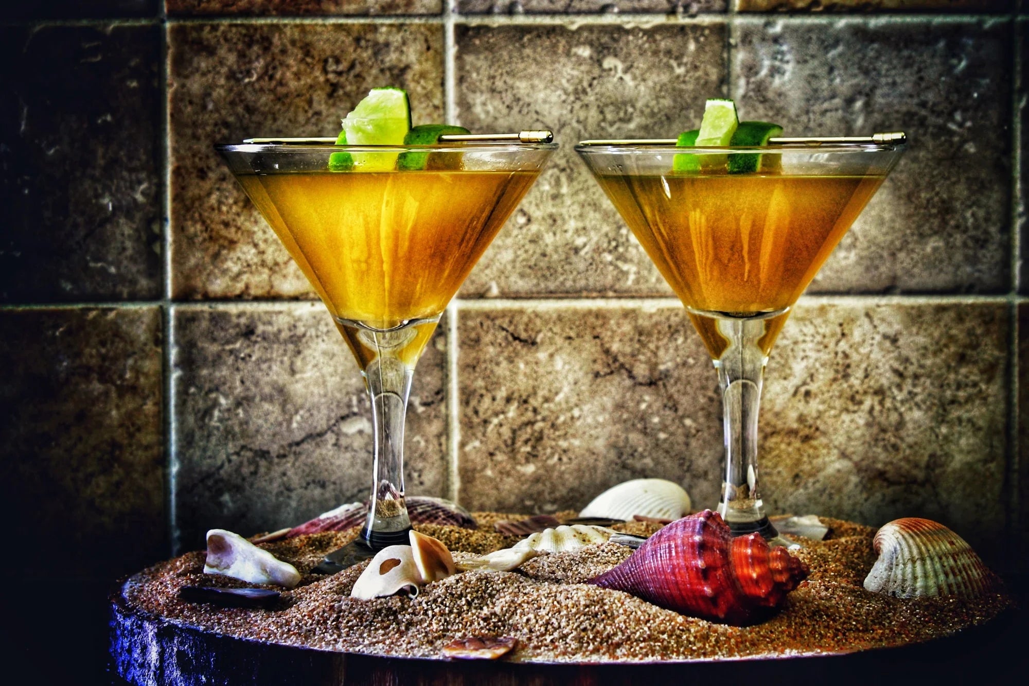 Pineapple Daiquiri made using Swan Knight Distillery golden spiced rum in 2 martini glasses on a bed of sand and shells